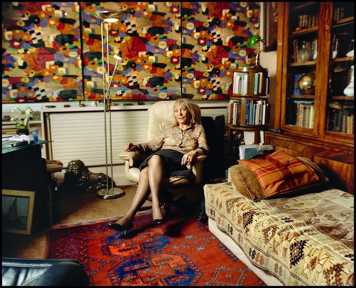 a woman sitting in a chair next to a bed and bookshelf filled with books