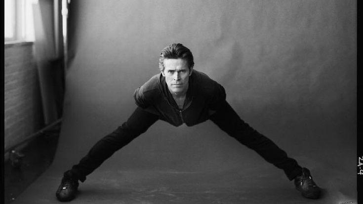 a man in black and white poses with his hands behind his head while leaning on one leg