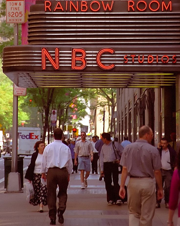 people are walking down the sidewalk in front of a theater marquee that reads rainbow room n b c