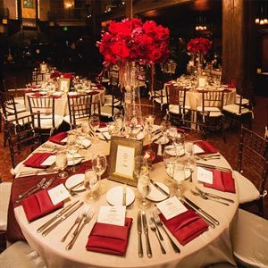 the table is set with red flowers and place settings for dinner or other special occasion