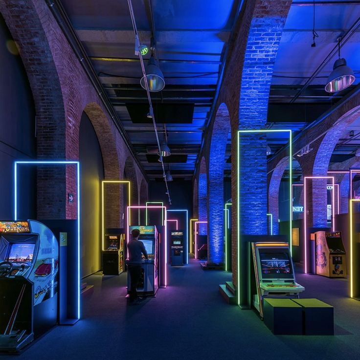 a room with arcade machines and neon colored lights on the walls, along with brick arches