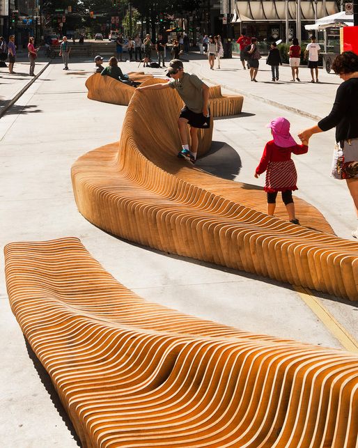 people are walking around an outdoor park with wooden benches and curved wood slats on the ground