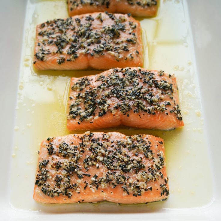 four salmon fillets with seasoning sit on a white platter, ready to be cooked