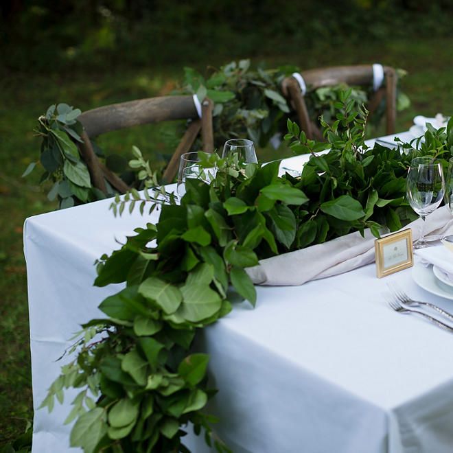 the table is set with white plates and silverware, greenery, and napkins