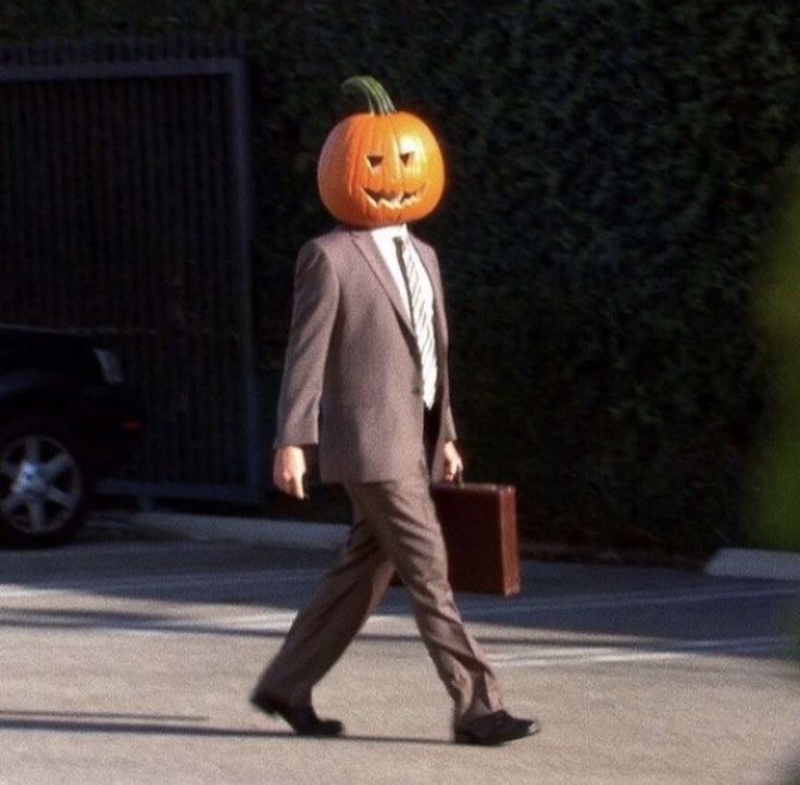 a man in a suit walks down the street with a pumpkin on his head