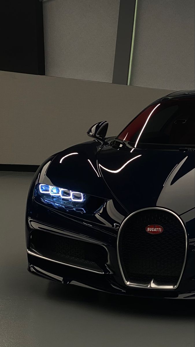 the front end of a black bugatti car with its lights on in a garage