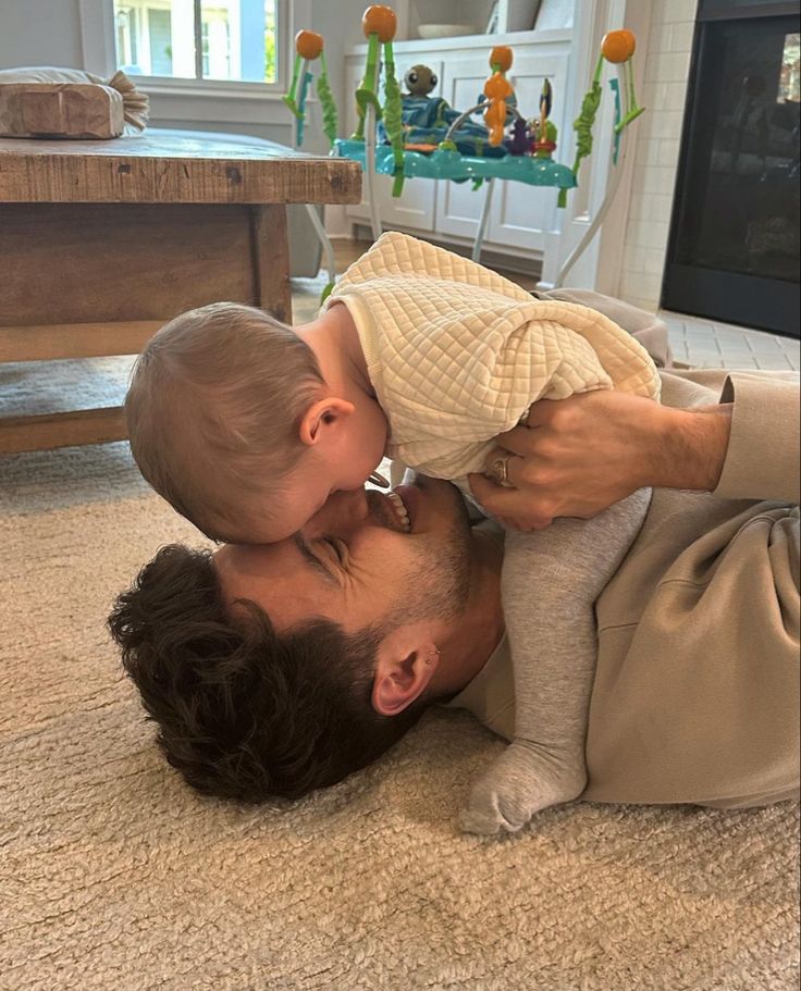 a man holding a baby up to his face while laying on the floor in front of a tv