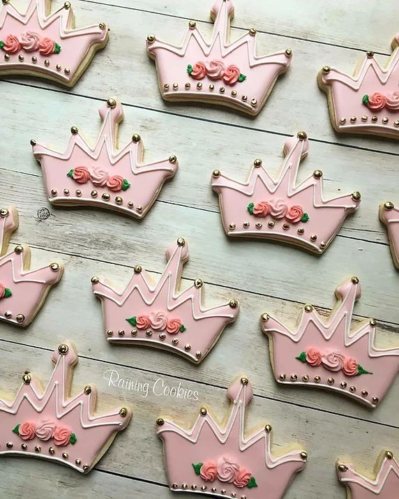 decorated cookies in the shape of crowns are displayed on a wooden table with pink frosting