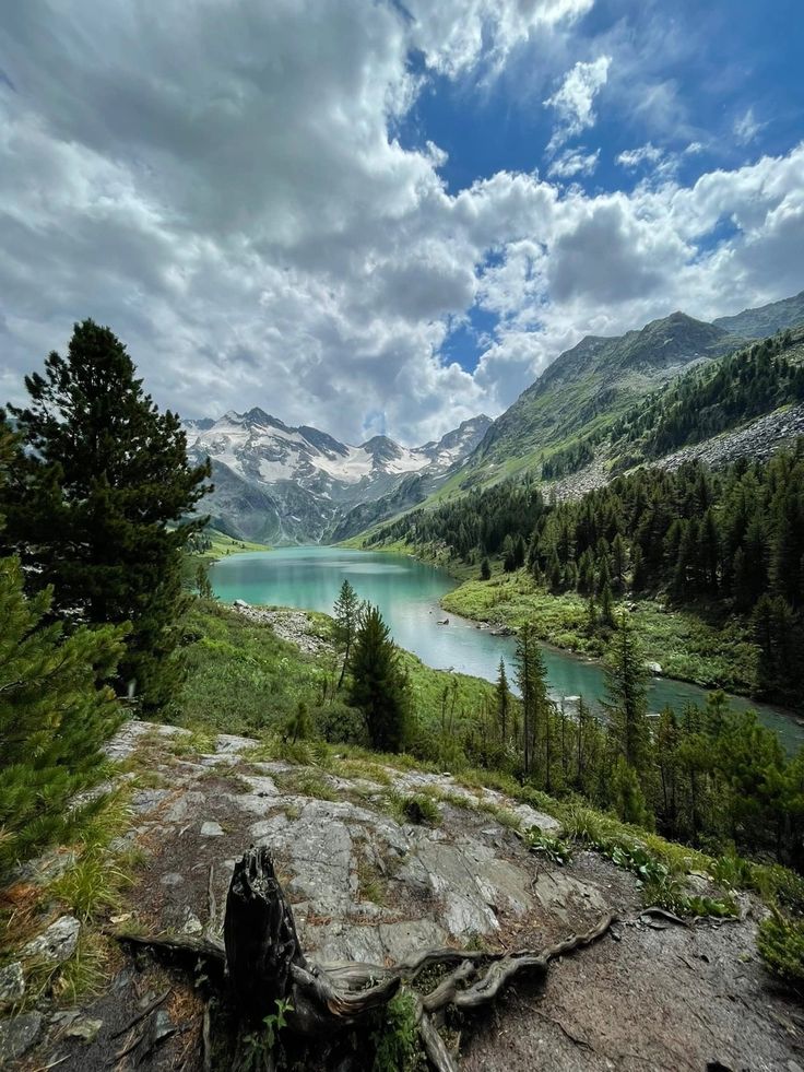 a lake surrounded by trees and mountains under a cloudy sky