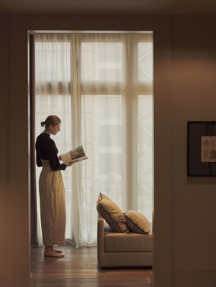 a woman standing in front of a window reading a book