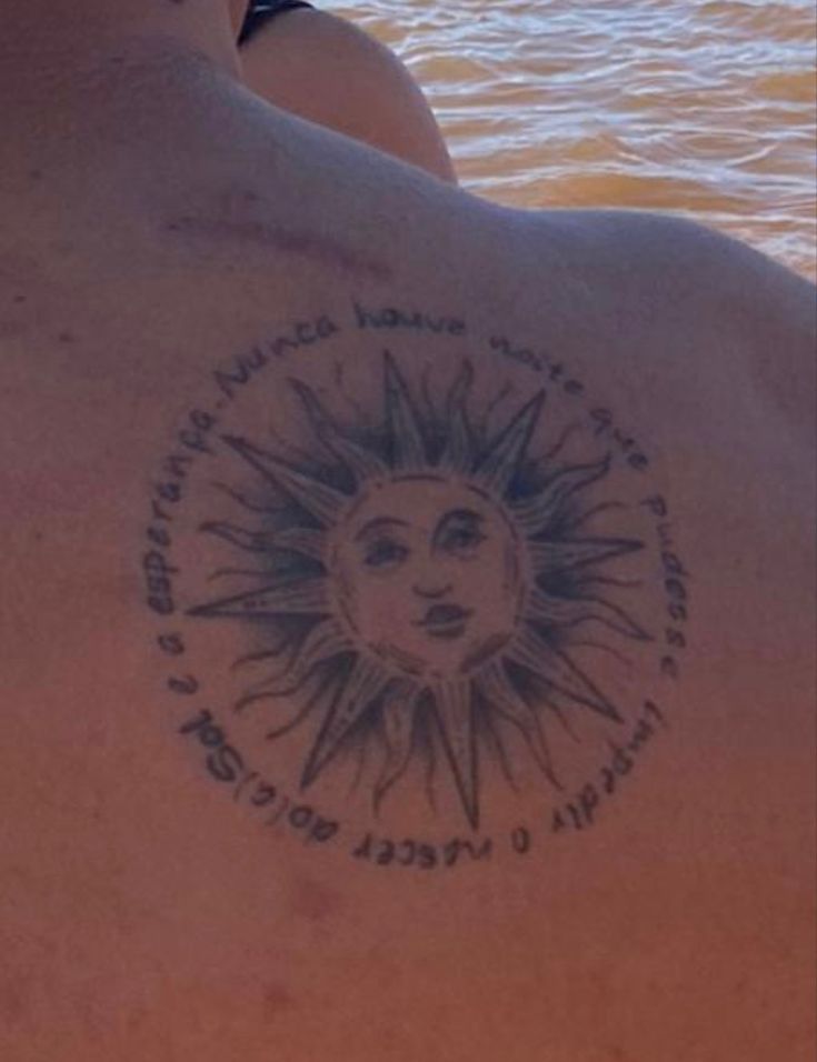 a man with a sun tattoo on his back sitting in the water looking out at the ocean