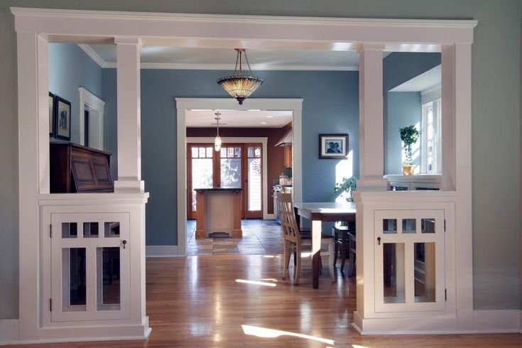 an open door leading to a dining room and living room with blue walls, hardwood floors and white columns