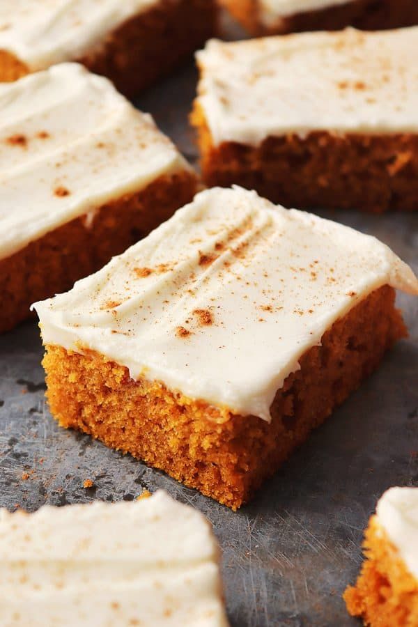 several pieces of carrot cake with white frosting on top sitting on a baking sheet