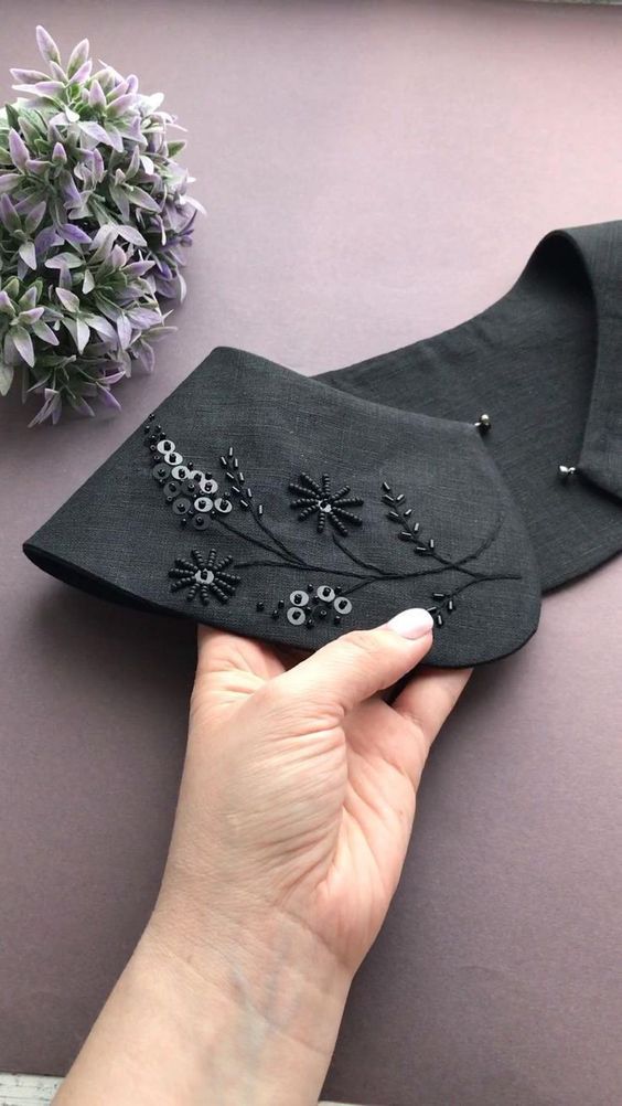 a hand holding a piece of black cloth with embroidered flowers and leaves on the side