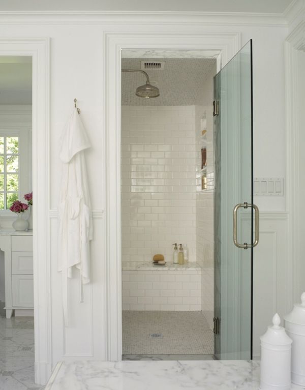 a white bathroom with marble flooring and glass shower door, along with two towels hanging on the wall