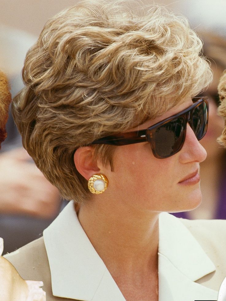 a woman wearing sunglasses and a white shirt is looking off to the side while she has her hair pulled back