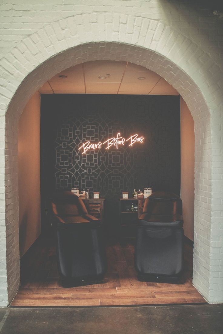 two black chairs sitting in front of a white brick wall with neon signs on it