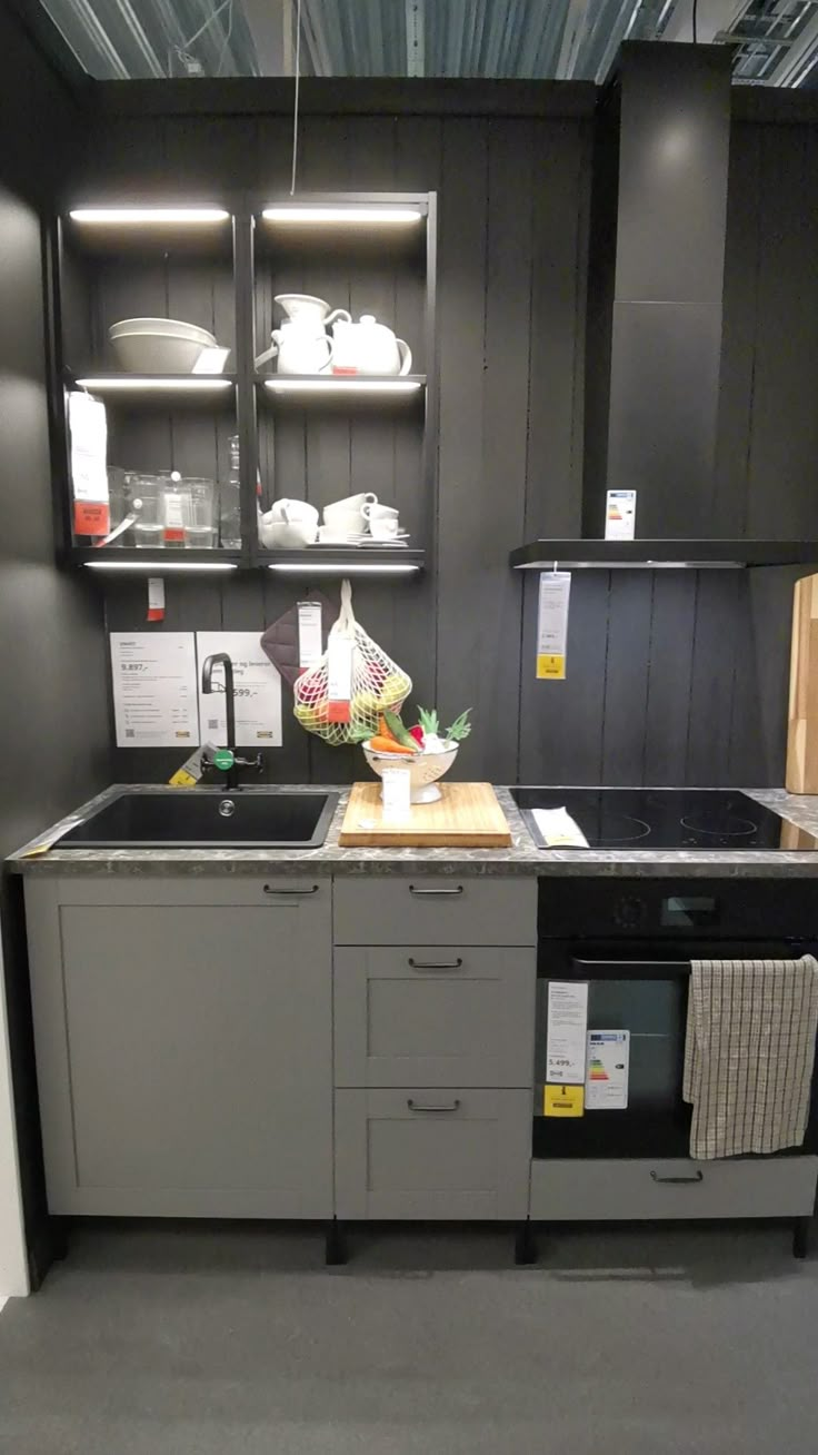 a kitchen with gray cabinets and black counter tops is shown in this image, there are dishes on the shelves above the sink