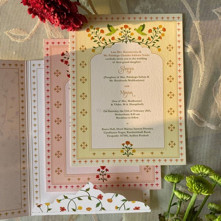 two wedding cards with flowers on them next to a vase filled with red carnations