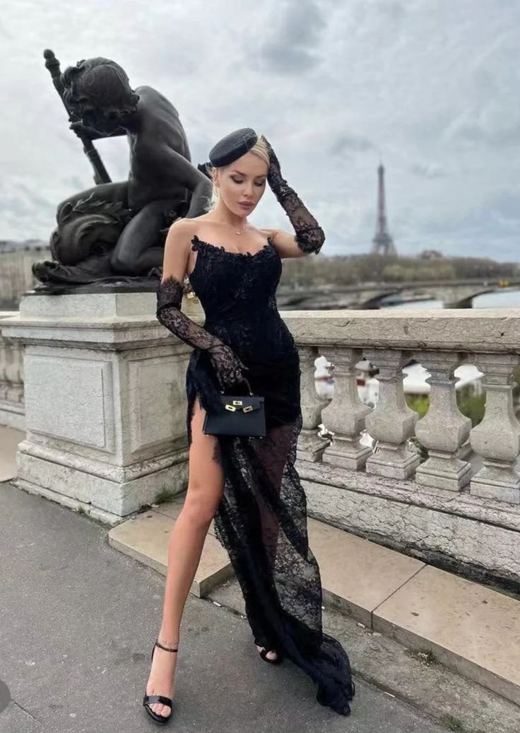 a woman standing on top of a bridge wearing a black dress and holding a purse