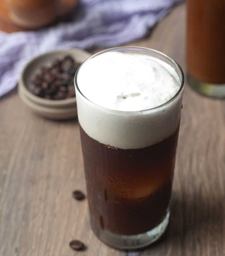 two glasses filled with liquid sitting on top of a wooden table next to coffee beans