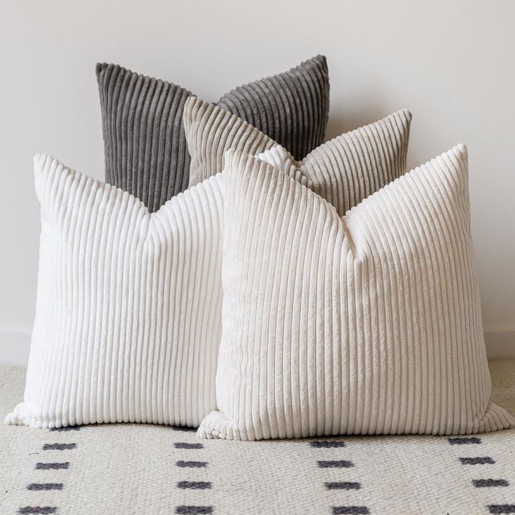 three pillows sitting on top of a bed next to each other in front of a white wall