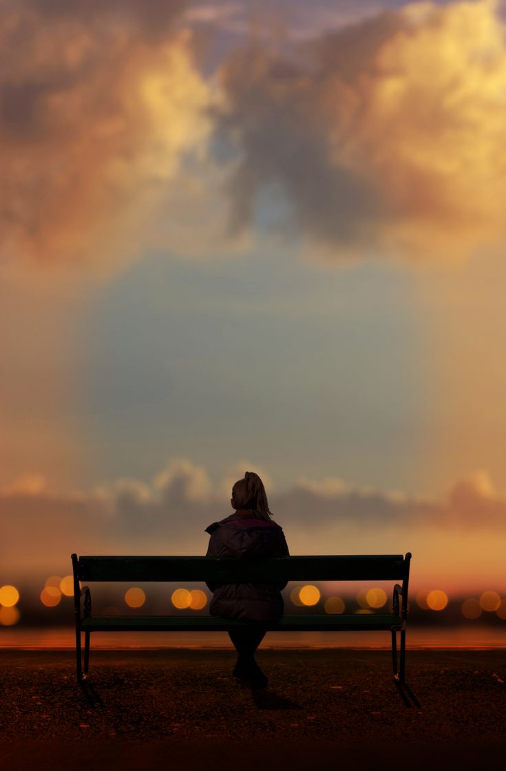 a person sitting on a bench in front of a sky filled with clouds and lights