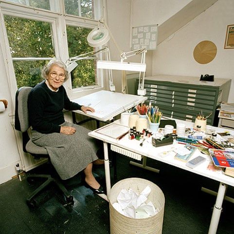 an older woman sitting at a desk in front of a window