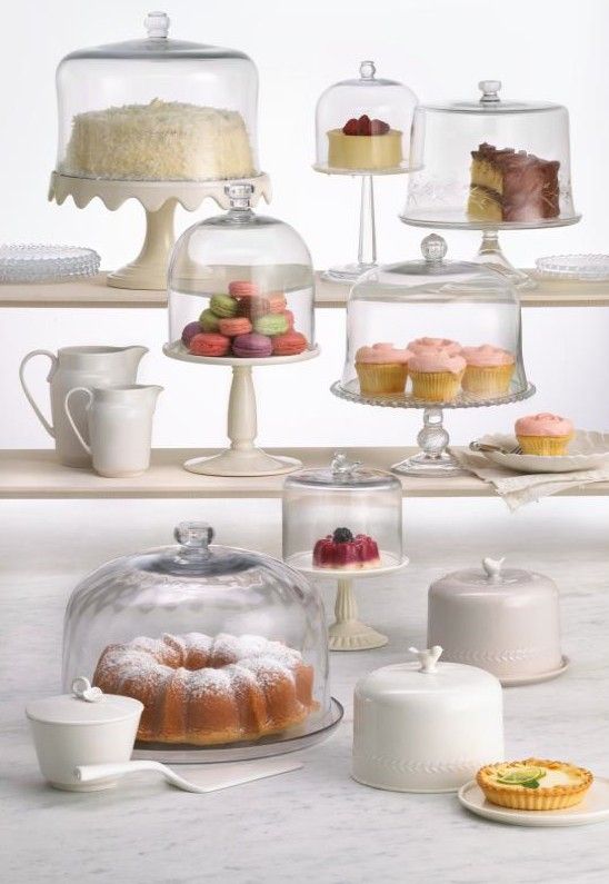 there are many cakes and cupcakes on the shelves in this kitchen, all under glass domes