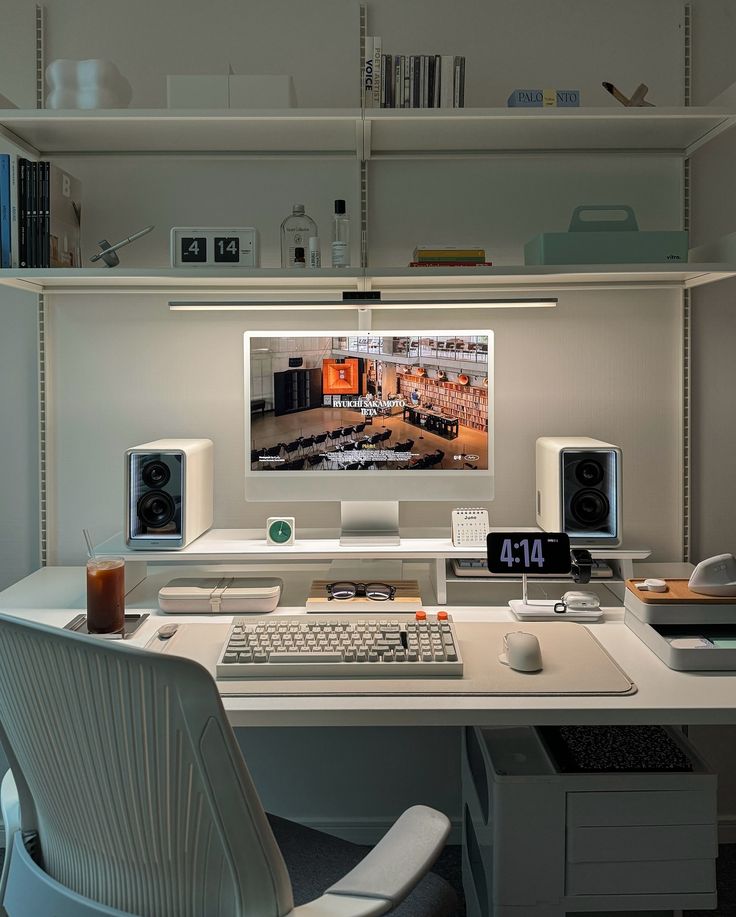 a computer desk topped with a monitor and keyboard next to a white shelf filled with books