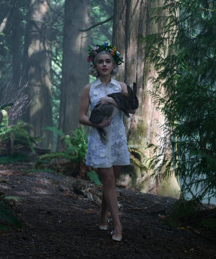 a woman in a white dress holding a black cat and wearing a wreath on her head