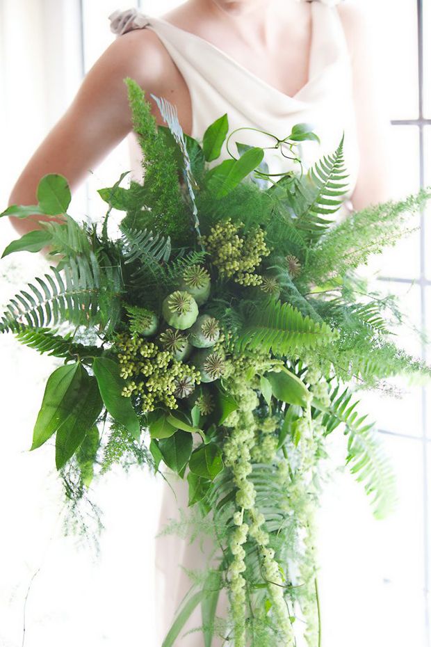 a woman in a white dress holding a large bouquet of green plants and foliages