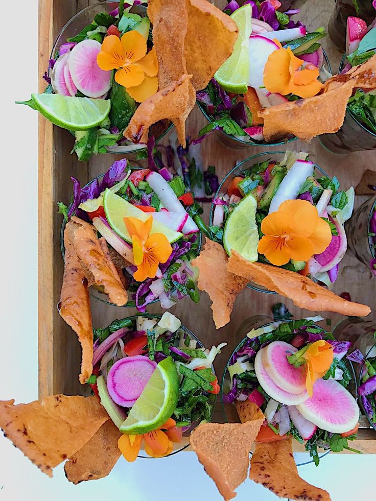 an arrangement of vegetables and tortilla chips arranged in a wooden tray on a white surface