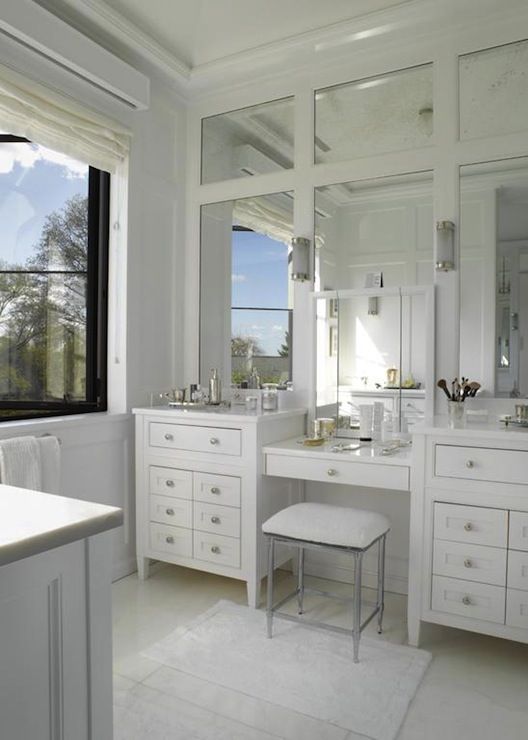 a white bathroom with two sinks, mirrors and stool in front of a large window