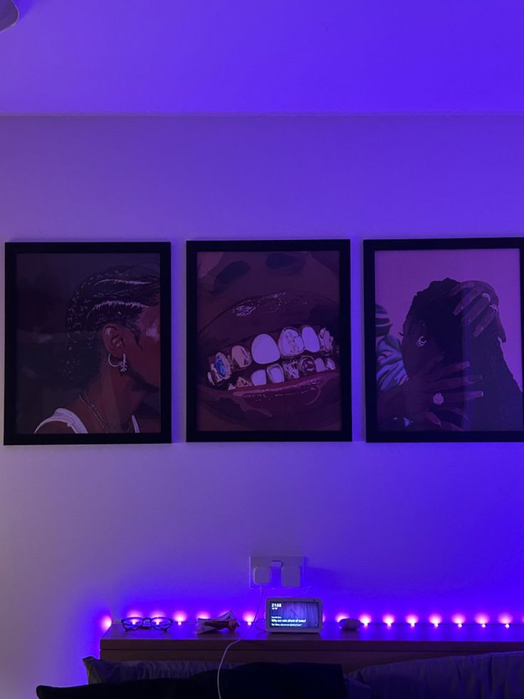 three framed pictures hang on the wall above a bed in a room with purple lighting