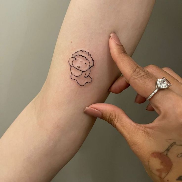 a person holding their arm with a small tattoo on it's left side, and another hand that has a tiny drawing of a teddy bear