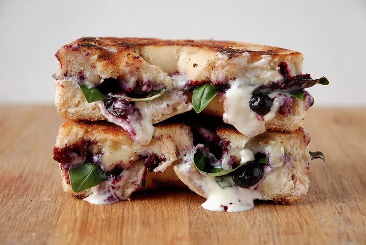 two grilled cheese sandwiches stacked on top of each other with blueberries and spinach