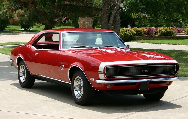 a red muscle car is parked in the driveway