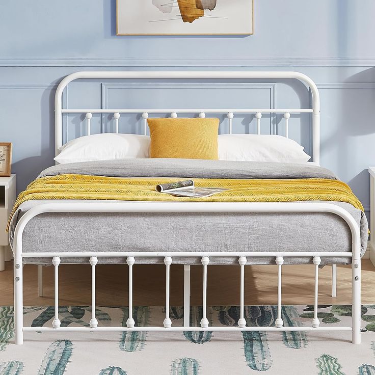 a white metal bed frame with yellow pillows and blankets on it in a blue bedroom