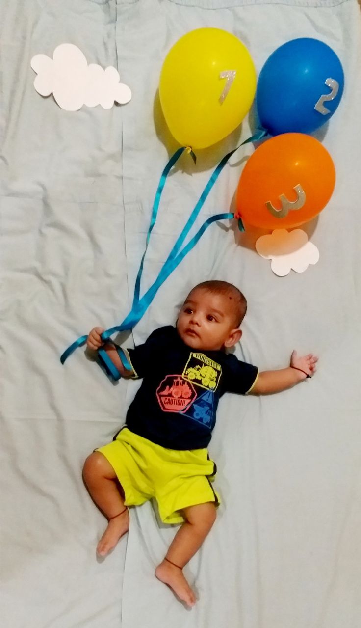 a baby laying on top of a bed next to balloons