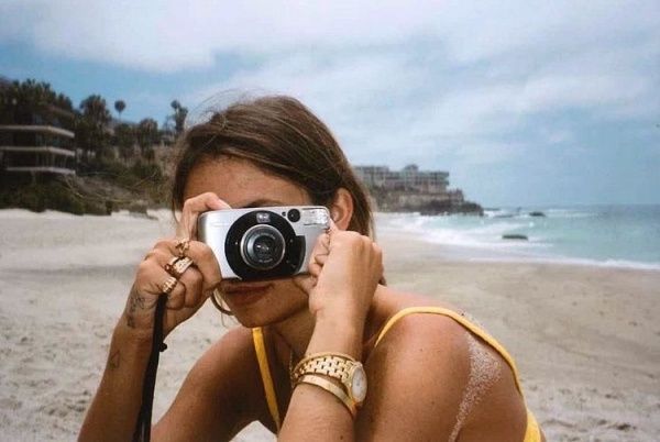 a woman taking a photo on the beach with her camera in front of her face