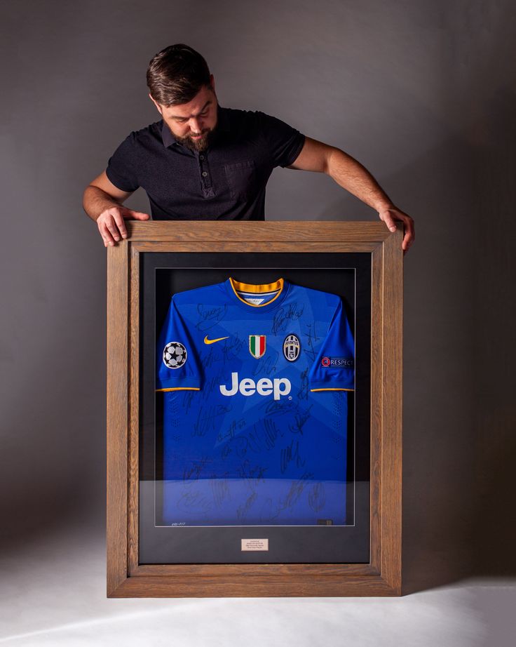 a man holding a framed jersey in front of a gray background with his hands on the frame