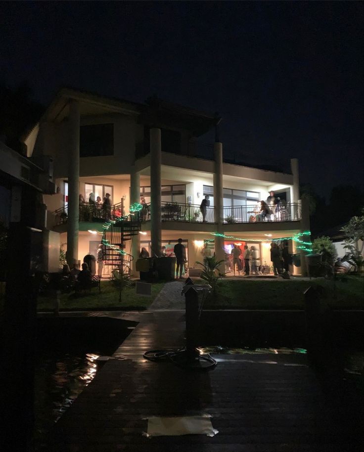 people are standing on the balcony at night in front of a large house with columns