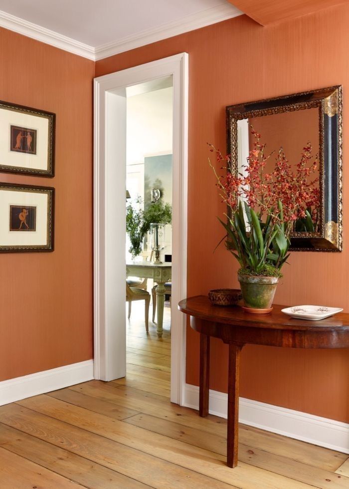 a room with orange walls and wooden flooring has a table, framed pictures on the wall