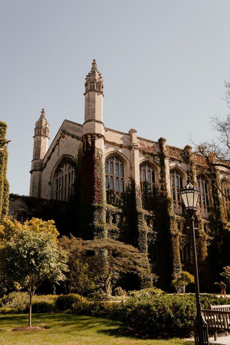 an old building with ivy growing on it's side and a park bench in the foreground