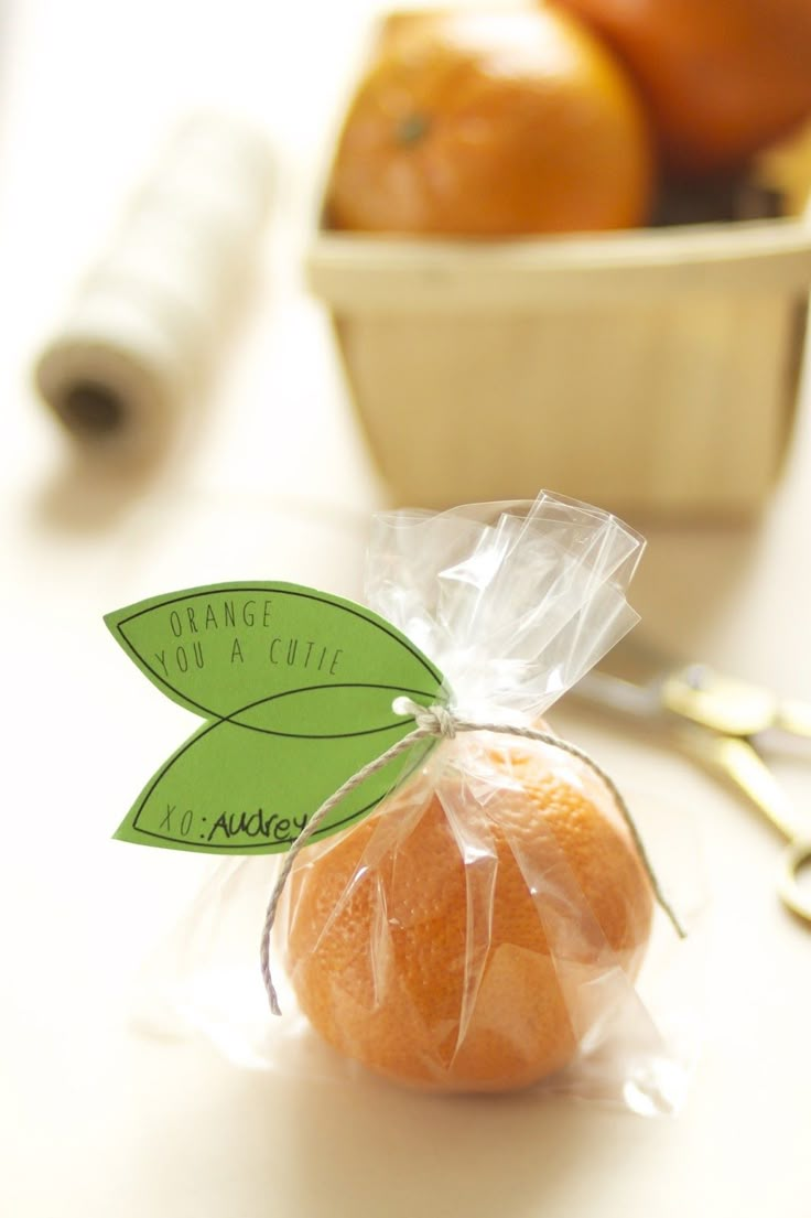 an orange wrapped in plastic sitting on a table next to some scissors and a bowl