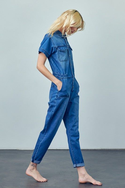 Marci Coverall - Medium Wash Denim Product Description: Elevate your casual wardrobe with the Marci Coverall, a stylish and functional jumpsuit designed for everyday wear. Made from 100% cotton, this medium wash denim coverall offers a relaxed fit and a classic silhouette. The short sleeves, collared neck, and front button closure add a touch of timeless charm. Perfect for any occasion, the Marci Coverall combines comfort and style effortlessly, making it a versatile addition to your collection. Dark Wash Utility Denim Jumpsuit, Utility Style Dark Wash Denim Jumpsuit, Spring Utility Denim Jumpsuit With Short Sleeves, Spring Short Sleeve Utility Denim Jumpsuit, Medium Wash Relaxed Fit Denim Utility Jumpsuit, Utility Washed Overalls Jumpsuit, Washed Blue Denim Jumpsuit With Pockets, Utility Denim Jumpsuit In Washed Blue With Pockets, Utility Washed Blue Denim Jumpsuit With Pockets