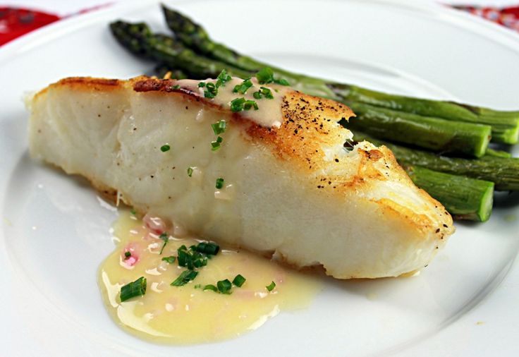 a piece of fish and asparagus on a white plate with yellow sauce, garnished with parsley