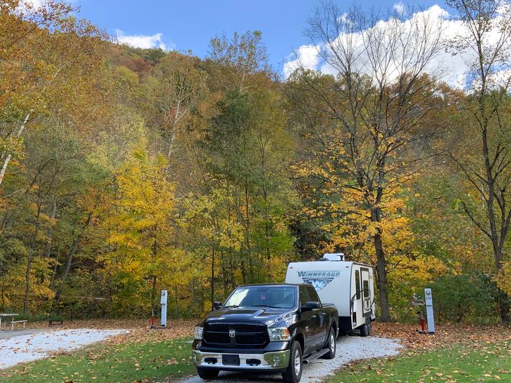 a truck is parked next to a camper in the woods with fall leaves on the ground