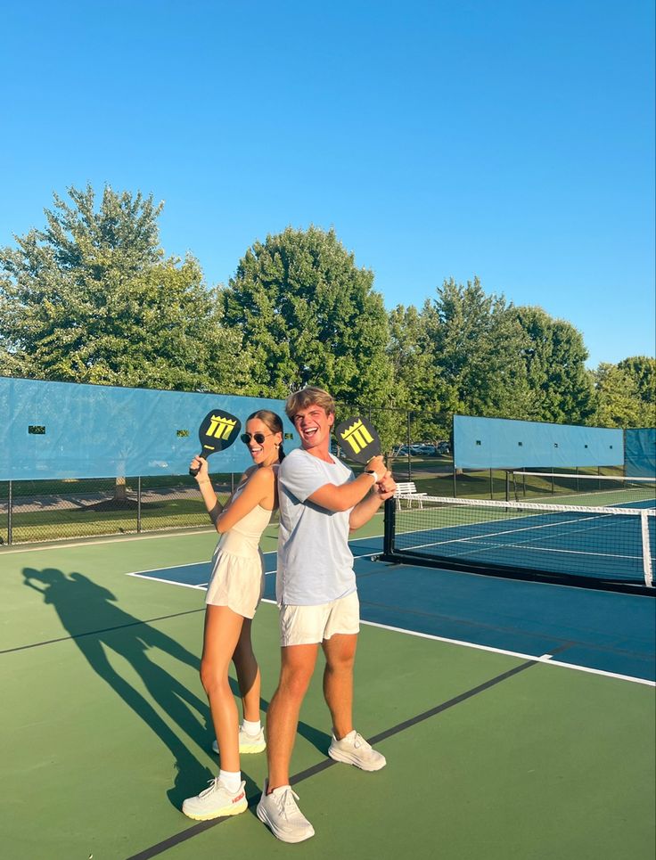 two people standing on a tennis court holding racquets and posing for the camera